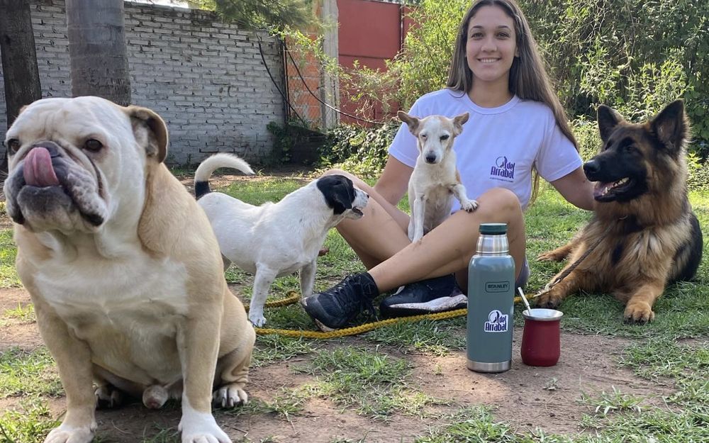 Malena de Del Arrabal tomando mate en el pasto rodeada de cuatro perros tranquilos en la hotelería